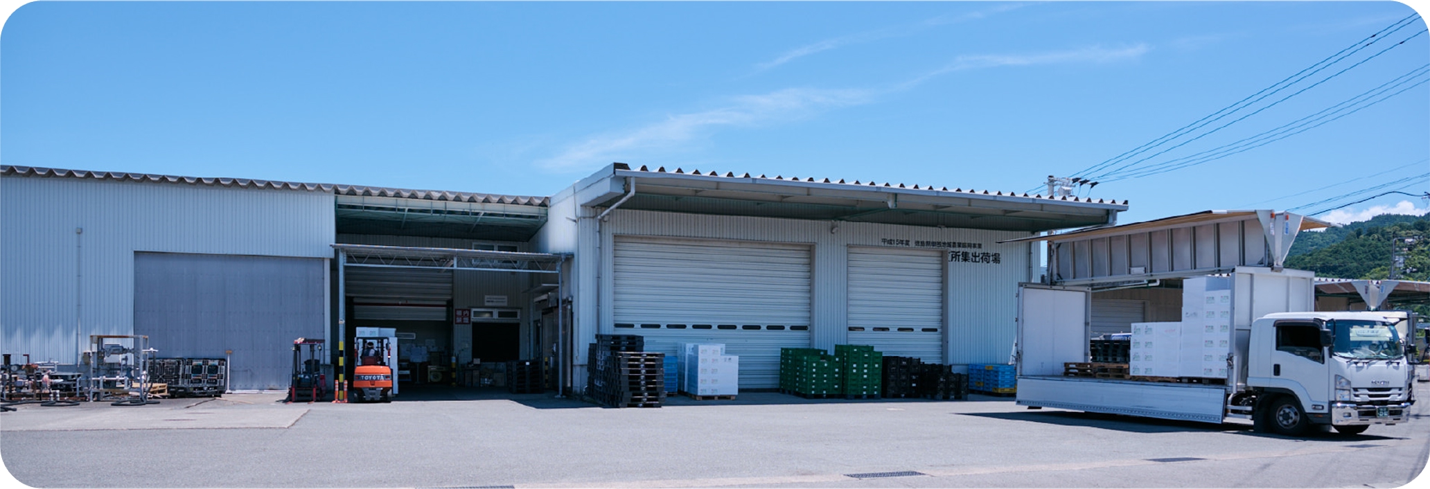 青空と南部しいたけパックセンターの外観。外には出荷用のトラックが止まっている。